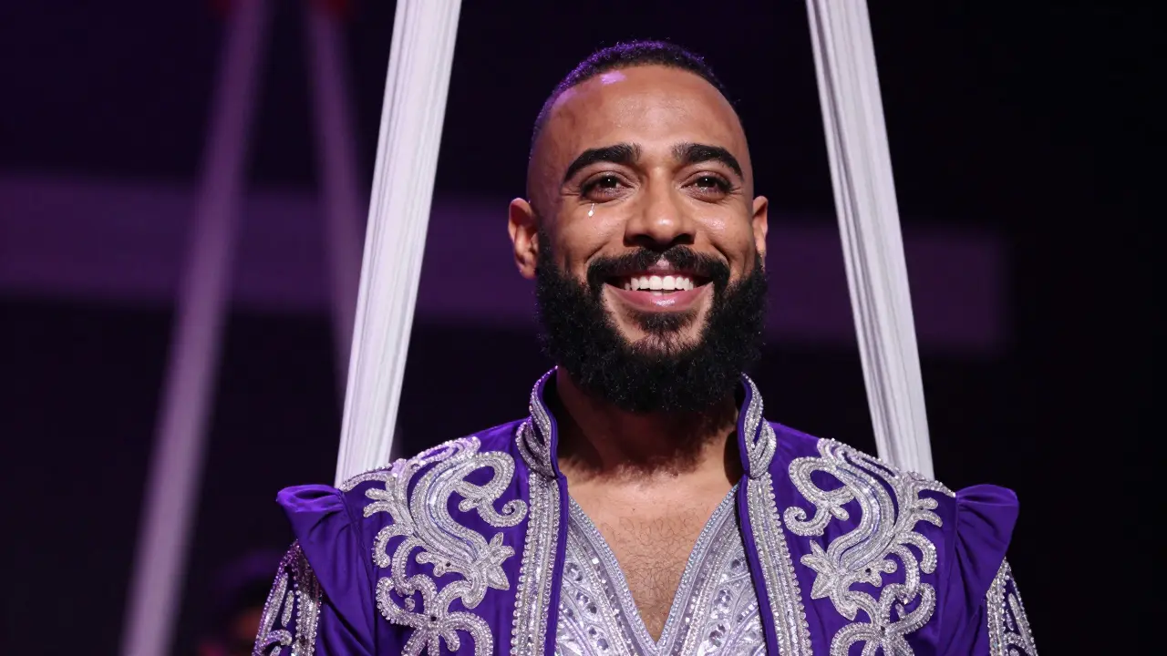 Performer with beard smiling confidently in glittering costume.